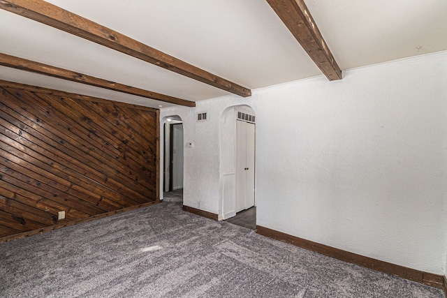 empty room featuring arched walkways, wooden walls, visible vents, dark colored carpet, and beamed ceiling