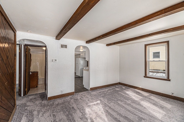 carpeted spare room featuring baseboards, visible vents, arched walkways, and beam ceiling