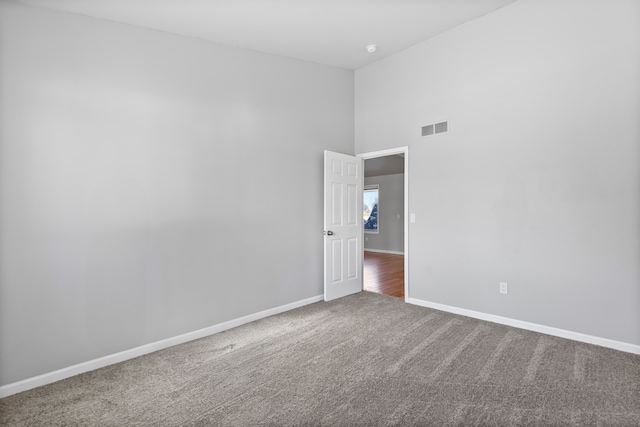 carpeted empty room with a towering ceiling, baseboards, and visible vents