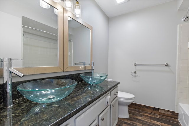 full bath featuring double vanity, wood finish floors, a sink, and toilet