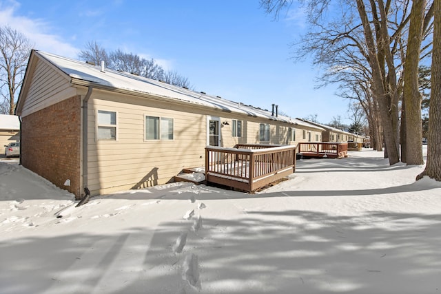 snow covered property with brick siding and a wooden deck