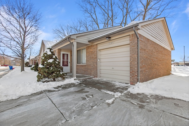 snow covered property featuring a garage and brick siding