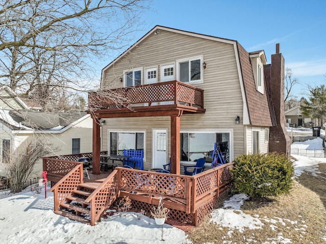 snow covered rear of property featuring a balcony, roof with shingles, a chimney, and a gambrel roof