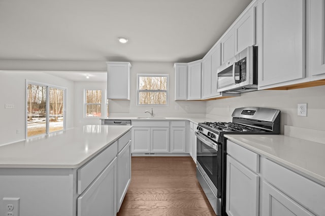 kitchen featuring light countertops, appliances with stainless steel finishes, white cabinets, a sink, and wood finished floors