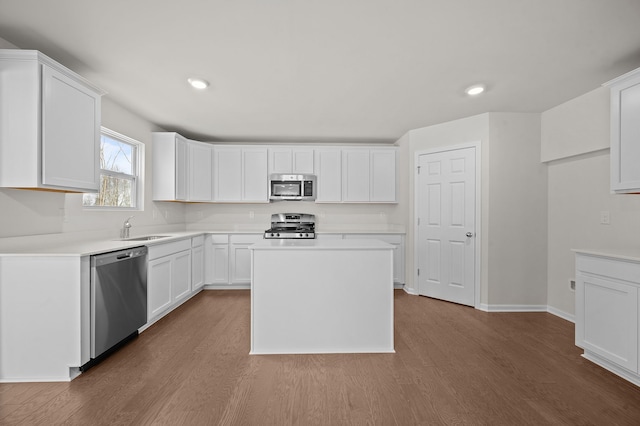 kitchen with light countertops, appliances with stainless steel finishes, white cabinets, a sink, and wood finished floors