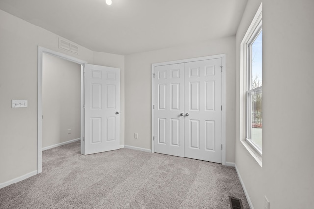 unfurnished bedroom featuring light carpet, a closet, visible vents, and baseboards