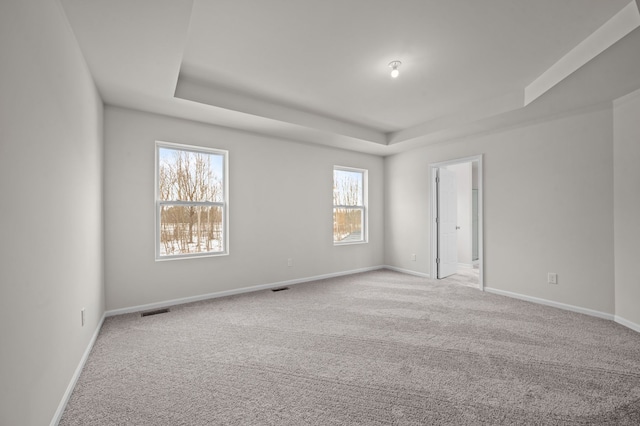 unfurnished room with light colored carpet, a raised ceiling, visible vents, and baseboards