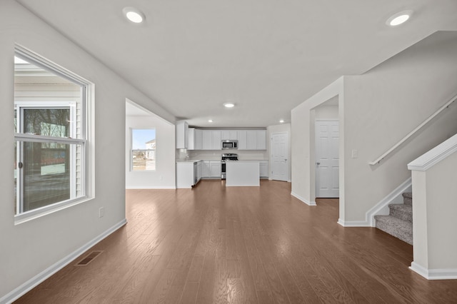 unfurnished living room with dark wood-style floors, recessed lighting, visible vents, and stairway