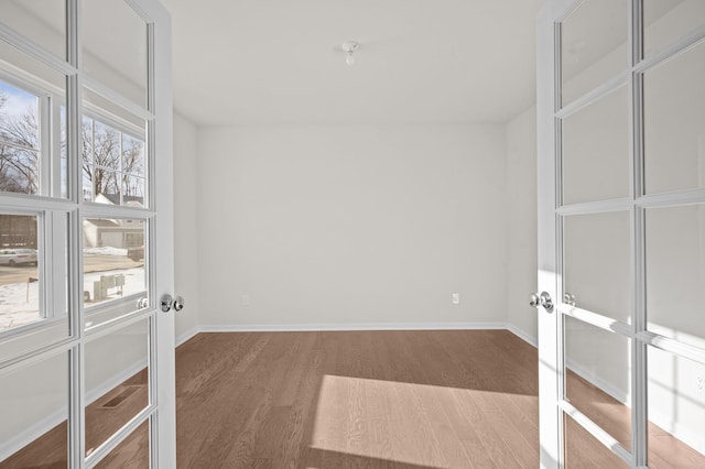 unfurnished room featuring baseboards, wood finished floors, a wealth of natural light, and french doors