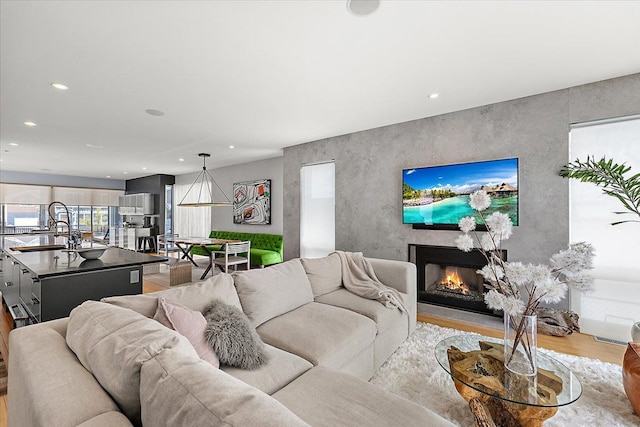 living area with light wood-style floors, recessed lighting, an accent wall, and a lit fireplace