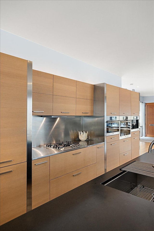 kitchen with tasteful backsplash, dark countertops, stainless steel appliances, light brown cabinets, and modern cabinets