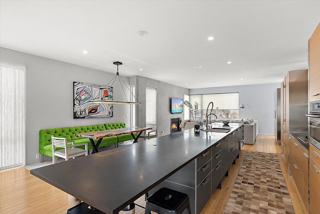 kitchen with dark countertops, a sink, a lit fireplace, and a center island with sink