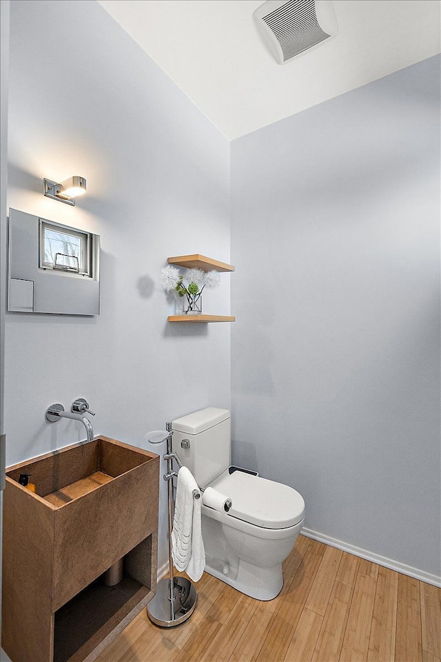 half bathroom with baseboards, visible vents, toilet, wood finished floors, and a sink