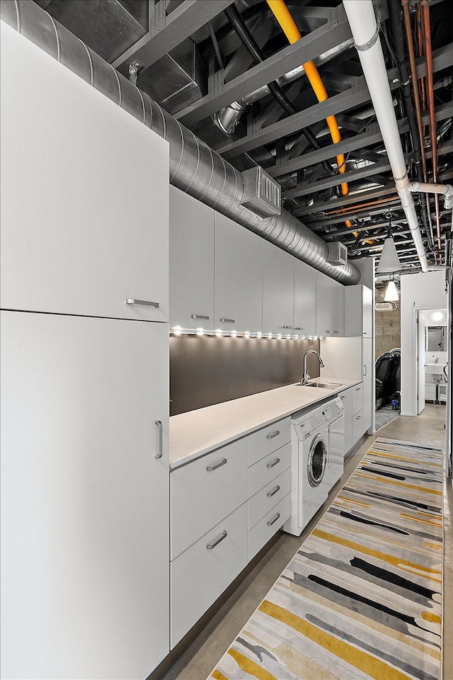 kitchen with light countertops, white cabinets, a sink, modern cabinets, and washer / dryer