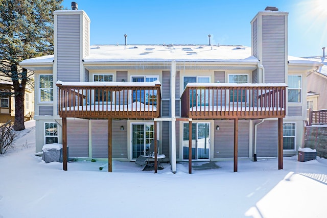 snow covered house featuring a deck and a chimney