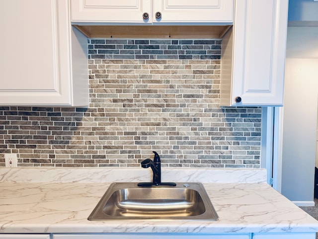 kitchen with tasteful backsplash, a sink, light stone countertops, and white cabinets