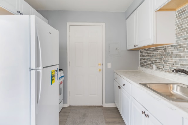 kitchen with tasteful backsplash, freestanding refrigerator, white cabinets, and a sink