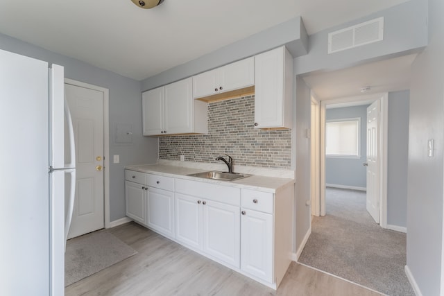 kitchen with visible vents, white cabinets, freestanding refrigerator, light countertops, and a sink