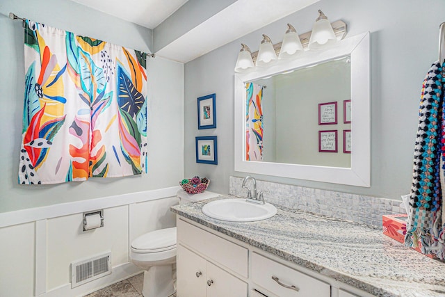 bathroom featuring visible vents, a decorative wall, toilet, wainscoting, and vanity