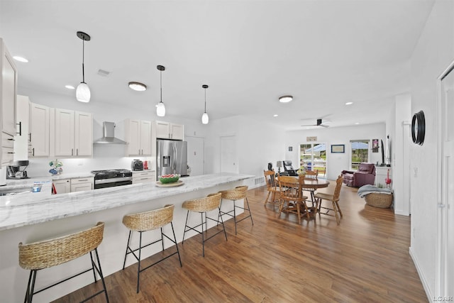 kitchen with wall chimney exhaust hood, open floor plan, stainless steel appliances, a kitchen bar, and white cabinetry