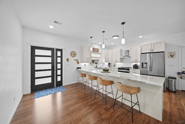 kitchen with a breakfast bar area, gas range oven, white cabinetry, wall chimney range hood, and stainless steel fridge