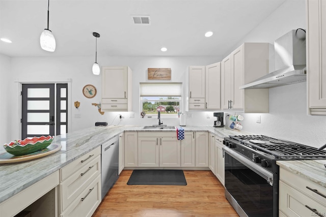 kitchen featuring visible vents, a sink, wall chimney range hood, stainless steel dishwasher, and gas stove