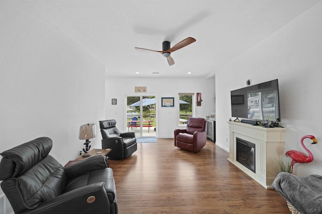 living room featuring recessed lighting, dark wood-type flooring, a ceiling fan, baseboards, and a glass covered fireplace