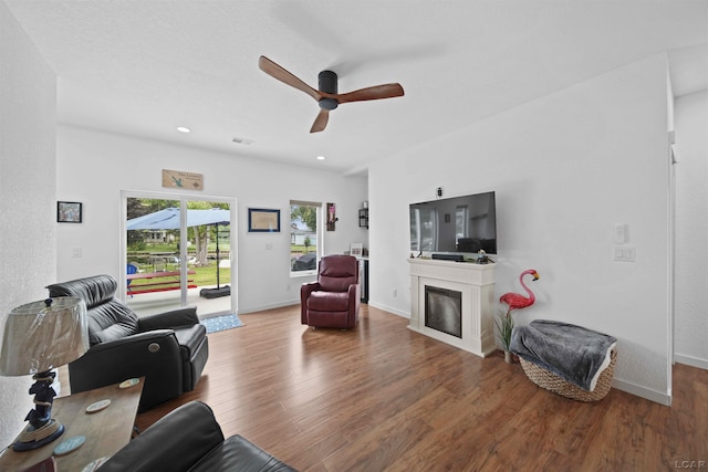 living room with baseboards, a ceiling fan, wood finished floors, and a glass covered fireplace