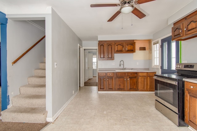 kitchen with light countertops, brown cabinetry, electric range, a ceiling fan, and a sink
