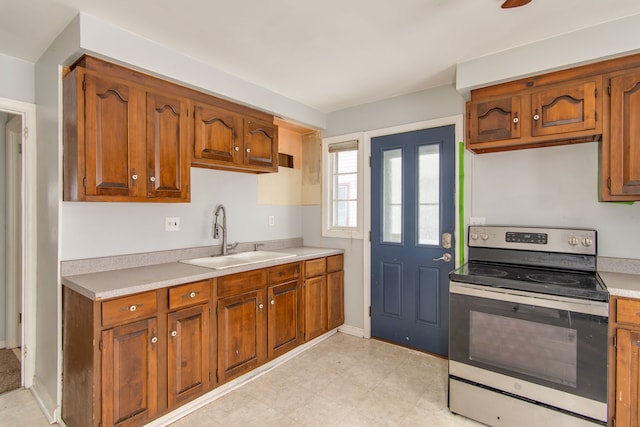 kitchen with brown cabinets, stainless steel electric range, light countertops, and a sink