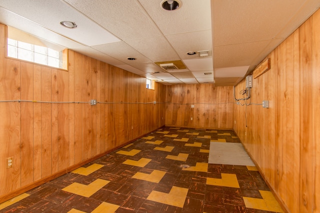 below grade area with tile patterned floors, visible vents, wood walls, and a drop ceiling