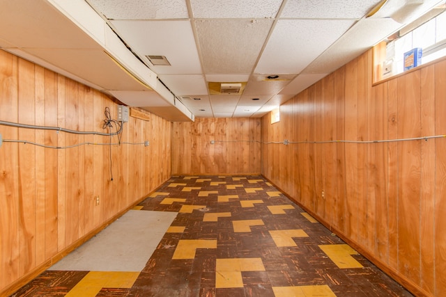 below grade area with tile patterned floors, visible vents, wooden walls, and a drop ceiling