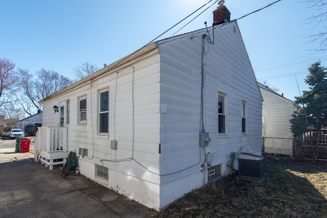view of side of home with central air condition unit, fence, and a chimney