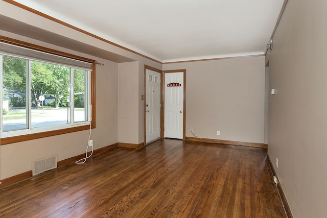 empty room featuring dark wood-style flooring, visible vents, and baseboards