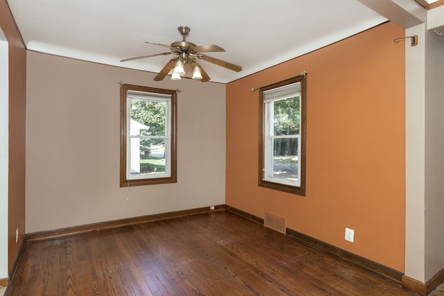 spare room featuring baseboards, dark wood-type flooring, visible vents, and a healthy amount of sunlight