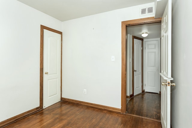 unfurnished room with dark wood-style floors, visible vents, and baseboards