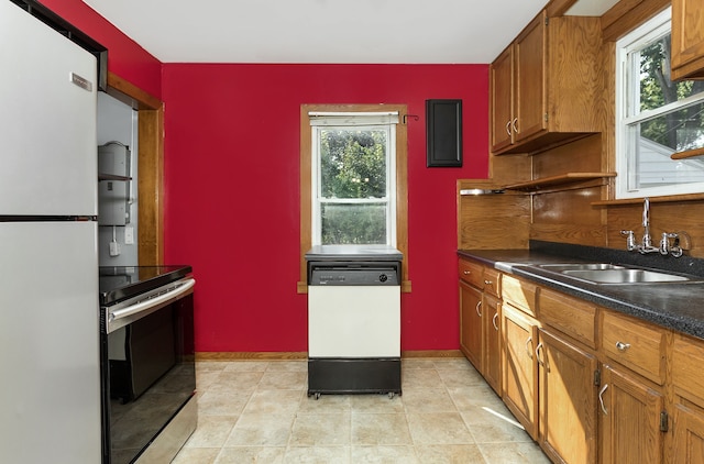 kitchen with white appliances, a sink, baseboards, brown cabinets, and dark countertops