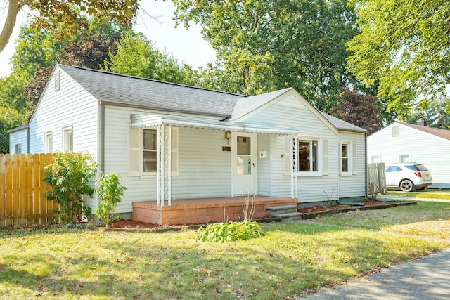 view of front facade featuring roof with shingles, a porch, a front lawn, and fence