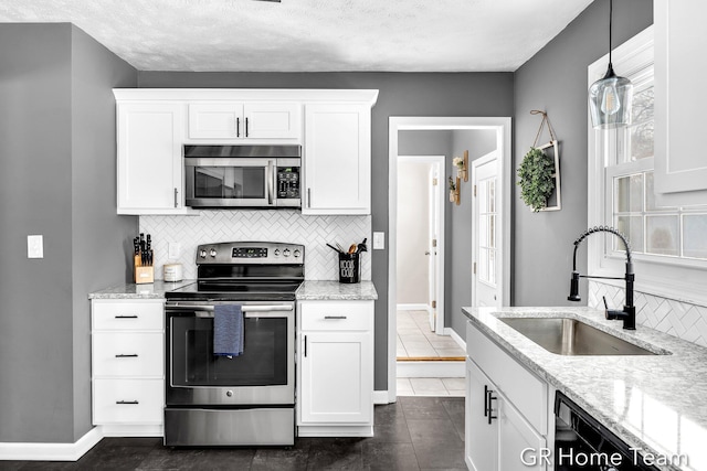 kitchen featuring appliances with stainless steel finishes, a sink, white cabinetry, and pendant lighting