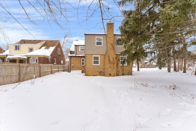 snow covered house featuring a chimney, fence, and brick siding