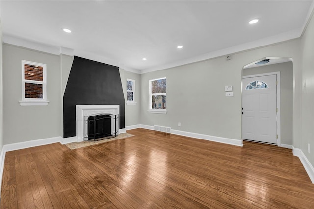 unfurnished living room featuring arched walkways, visible vents, a fireplace with flush hearth, wood finished floors, and baseboards