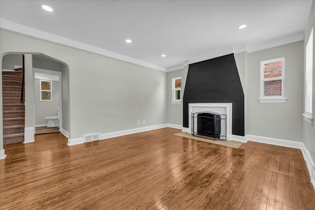 unfurnished living room with visible vents, arched walkways, a fireplace with flush hearth, stairway, and wood finished floors