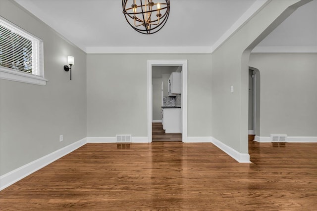 spare room featuring baseboards, visible vents, arched walkways, and wood finished floors