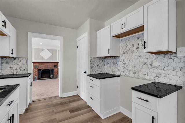 kitchen with white cabinetry, light wood-style floors, a brick fireplace, tasteful backsplash, and dark countertops