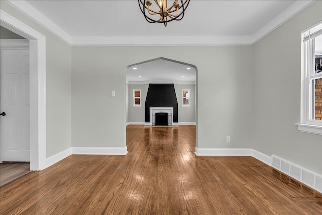 unfurnished living room with visible vents, a fireplace with raised hearth, baseboards, and wood finished floors