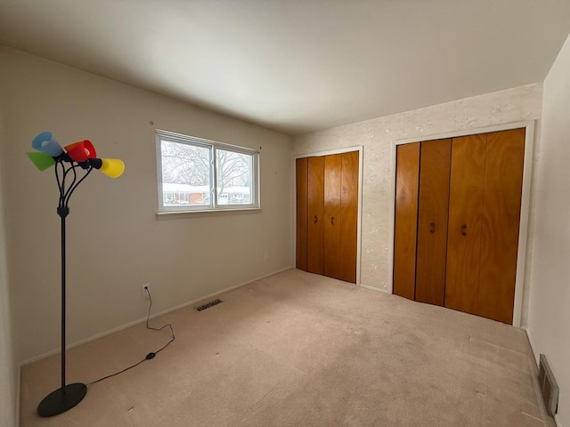 unfurnished bedroom with carpet, two closets, and visible vents