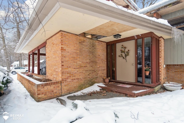 snow covered property entrance with brick siding