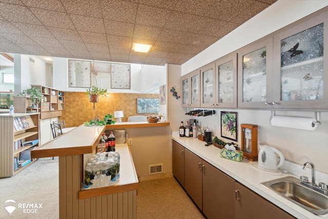 kitchen with visible vents, light countertops, a sink, and glass insert cabinets