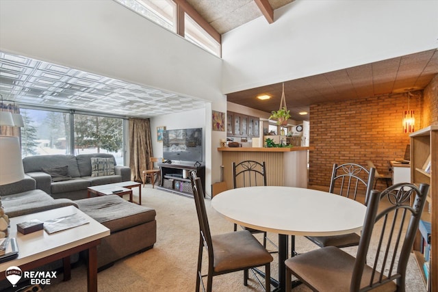 dining space with brick wall, light carpet, and a high ceiling