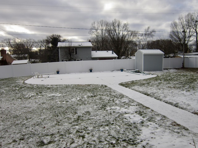 yard covered in snow with a storage shed, a fenced backyard, and an outbuilding